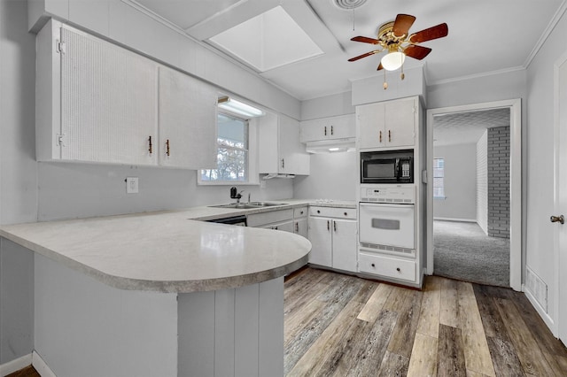 kitchen featuring black microwave, white oven, white cabinets, and kitchen peninsula