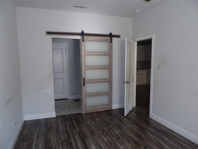 unfurnished bedroom with dark hardwood / wood-style floors and a barn door