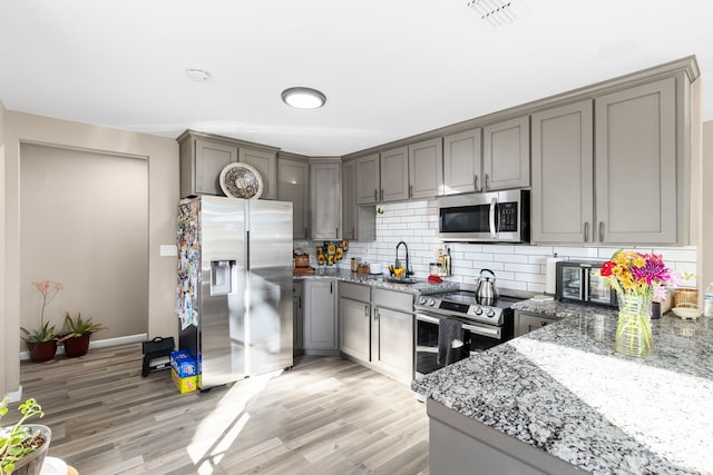 kitchen featuring light stone countertops, appliances with stainless steel finishes, light wood-type flooring, and gray cabinetry