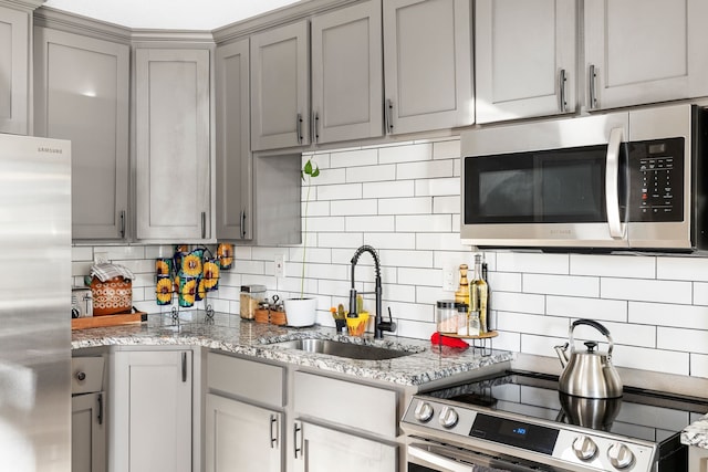 kitchen with gray cabinetry, sink, tasteful backsplash, light stone counters, and stainless steel appliances