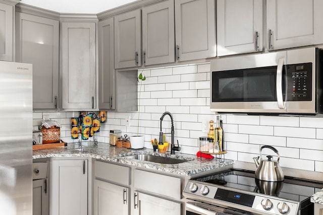 kitchen with sink, gray cabinets, stainless steel appliances, light stone counters, and decorative backsplash