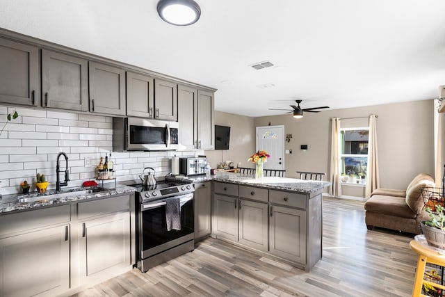 kitchen featuring kitchen peninsula, dark stone counters, stainless steel appliances, sink, and light hardwood / wood-style flooring