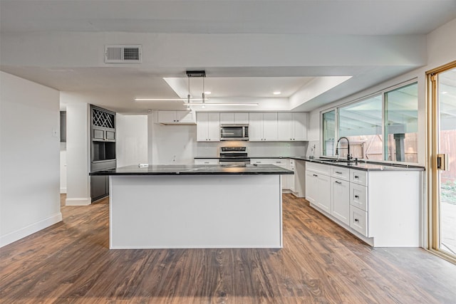 kitchen featuring appliances with stainless steel finishes, dark hardwood / wood-style flooring, pendant lighting, a center island, and white cabinetry