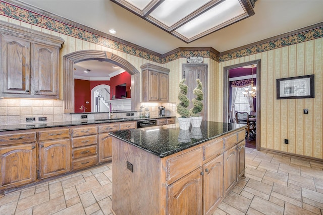 kitchen with a kitchen island, sink, a chandelier, dark stone counters, and ornamental molding