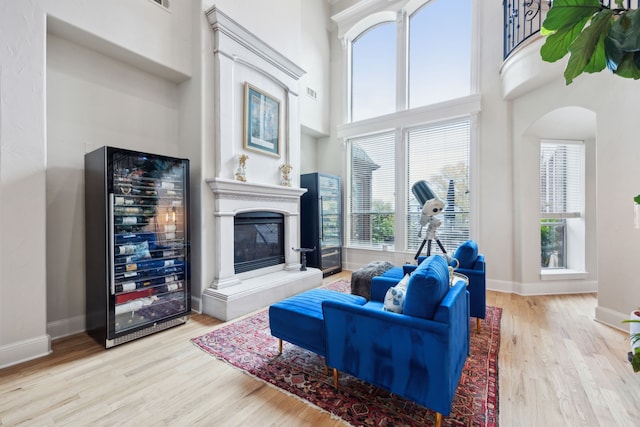 living room with wood finished floors, beverage cooler, baseboards, a towering ceiling, and a tiled fireplace