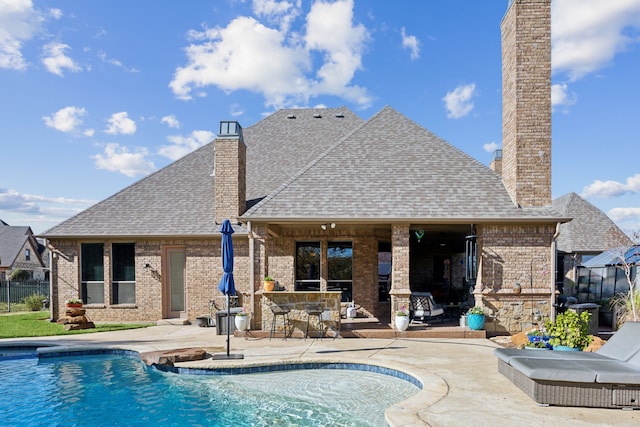 back of property featuring exterior bar, a patio, and a fenced in pool