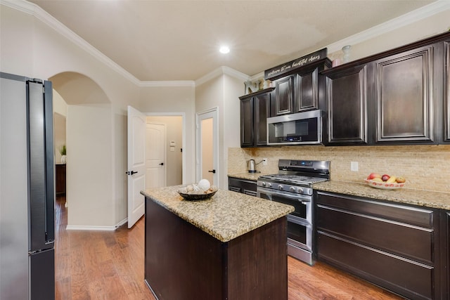 kitchen with light stone countertops, appliances with stainless steel finishes, dark brown cabinetry, a center island, and light hardwood / wood-style floors