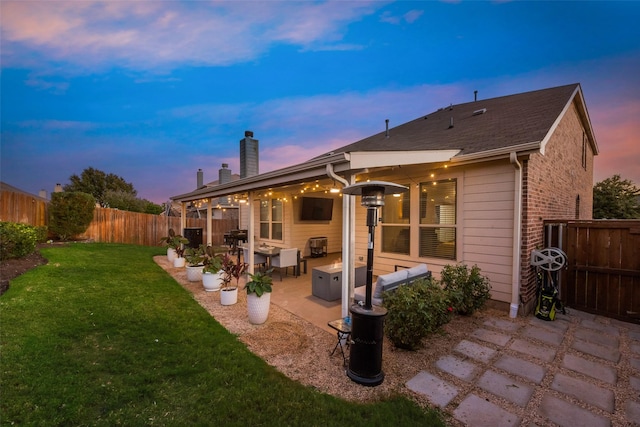 back house at dusk featuring a lawn and a patio area