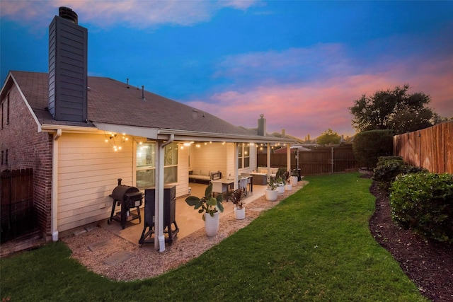 back house at dusk with a yard, exterior kitchen, and a patio