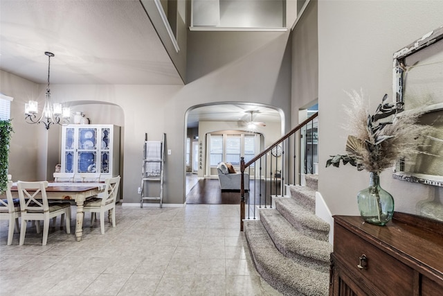 foyer entrance with baseboards, a chandelier, stairs, light tile patterned flooring, and arched walkways