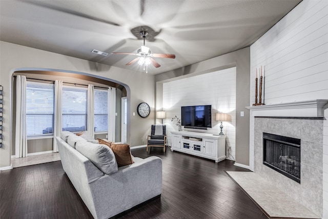 living room with a tile fireplace, dark hardwood / wood-style floors, and ceiling fan