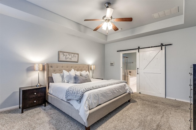 carpeted bedroom with a raised ceiling, ceiling fan, a barn door, and ensuite bath