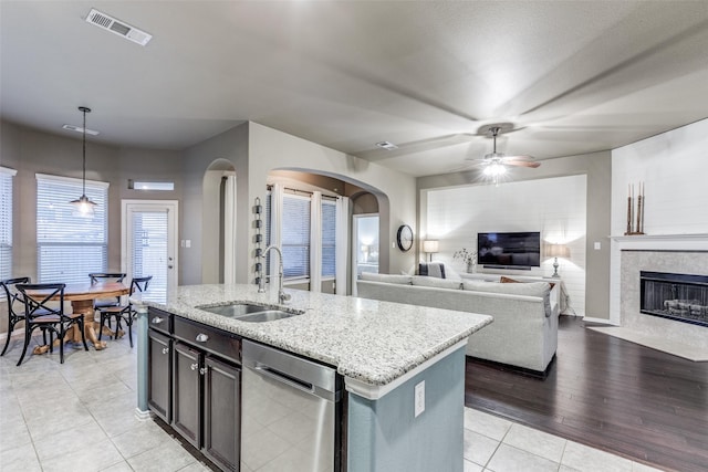 kitchen featuring sink, light stone counters, a center island with sink, dishwasher, and pendant lighting