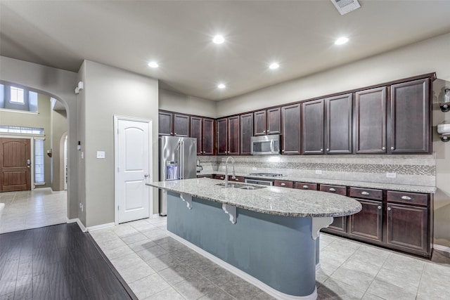 kitchen featuring light stone counters, a breakfast bar, arched walkways, a sink, and appliances with stainless steel finishes