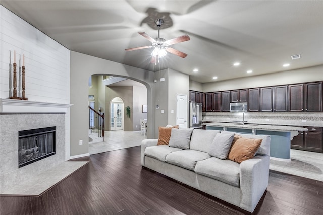 living room with a tiled fireplace, dark wood-type flooring, sink, and ceiling fan