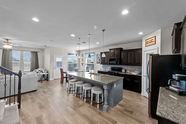 kitchen featuring sink, dark brown cabinets, hanging light fixtures, a kitchen island with sink, and black appliances