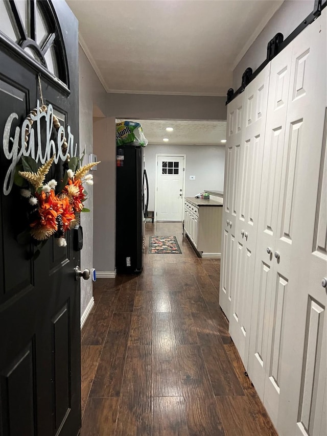 corridor featuring a barn door, dark hardwood / wood-style floors, and ornamental molding