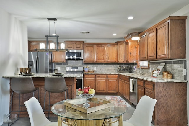 kitchen with pendant lighting, decorative backsplash, light stone countertops, and stainless steel appliances