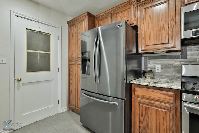 kitchen with light stone counters, light tile patterned floors, stainless steel appliances, and tasteful backsplash