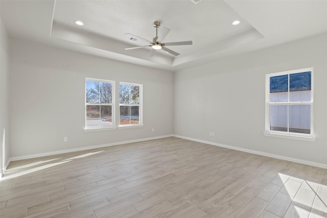 unfurnished room with ceiling fan, a tray ceiling, and light wood-type flooring