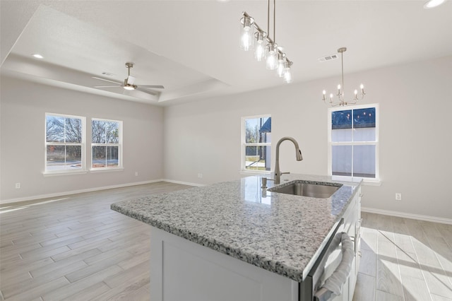 kitchen featuring sink, hanging light fixtures, a center island with sink, a raised ceiling, and white cabinets