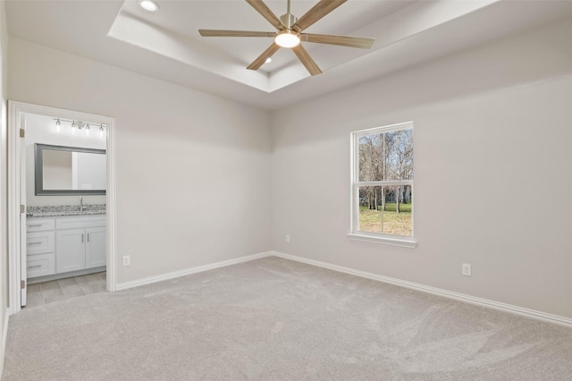 carpeted empty room with a tray ceiling, ceiling fan, and sink