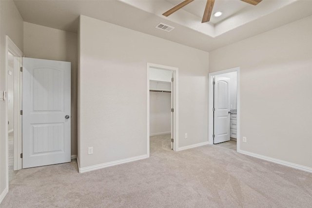 unfurnished bedroom featuring a spacious closet, light carpet, a raised ceiling, a closet, and ceiling fan