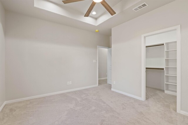 unfurnished bedroom with ceiling fan, a raised ceiling, light carpet, a spacious closet, and a closet