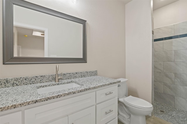 bathroom with vanity, toilet, wood-type flooring, and tiled shower