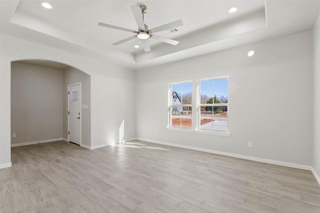 empty room featuring light wood-type flooring, a raised ceiling, and ceiling fan