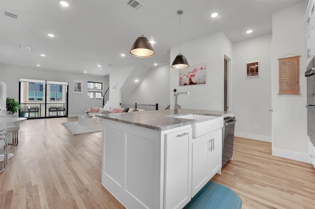 kitchen featuring white cabinets, decorative light fixtures, light hardwood / wood-style floors, and an island with sink