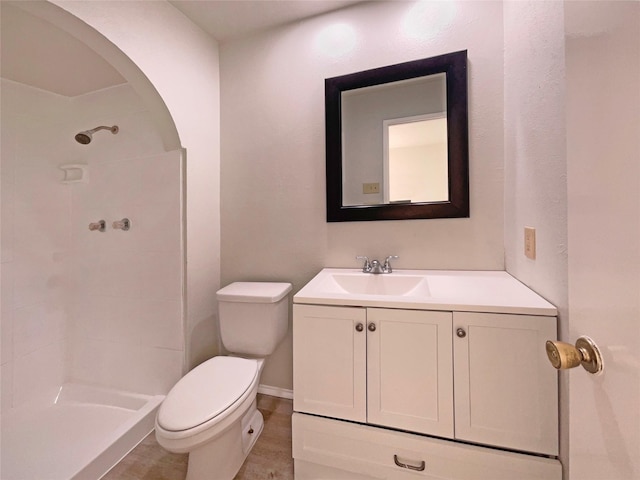 bathroom featuring a tile shower, vanity, and toilet