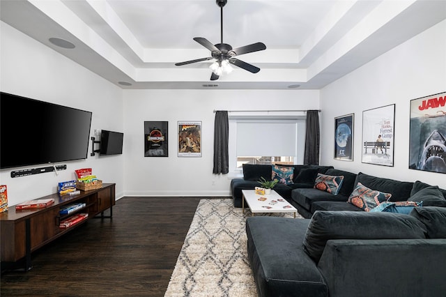 living room featuring dark wood-type flooring, ceiling fan, and a tray ceiling