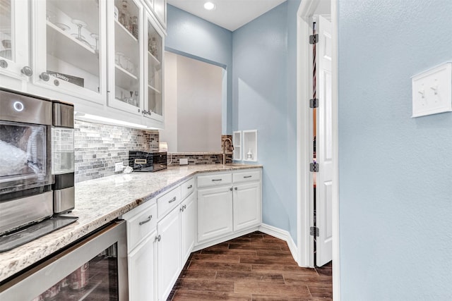 kitchen with light stone countertops, backsplash, beverage cooler, dark hardwood / wood-style floors, and white cabinetry