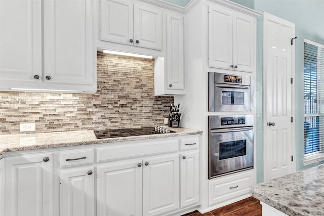 kitchen featuring black electric stovetop, stainless steel oven, white cabinets, and light stone counters