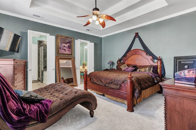 carpeted bedroom with ceiling fan, ornamental molding, a tray ceiling, and ensuite bath