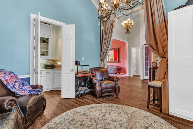 living area featuring ornamental molding, a towering ceiling, an inviting chandelier, and dark hardwood / wood-style flooring