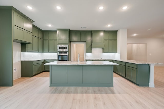 kitchen featuring appliances with stainless steel finishes, light wood-type flooring, green cabinetry, and backsplash