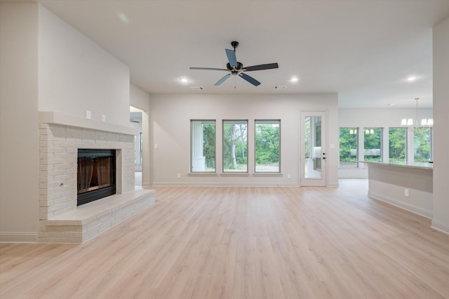 unfurnished living room featuring a fireplace, ceiling fan with notable chandelier, and light hardwood / wood-style flooring