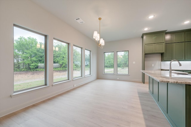 kitchen with sink, light hardwood / wood-style flooring, green cabinetry, decorative light fixtures, and light stone counters