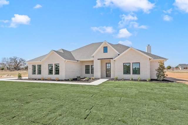 modern inspired farmhouse featuring a front yard, brick siding, a chimney, and roof with shingles