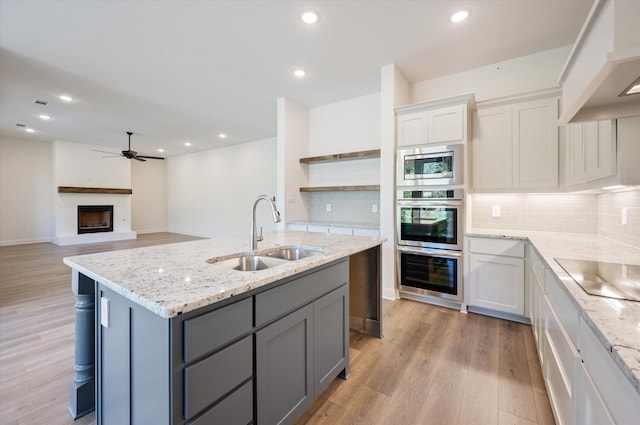 kitchen featuring appliances with stainless steel finishes, light wood-type flooring, backsplash, sink, and white cabinetry