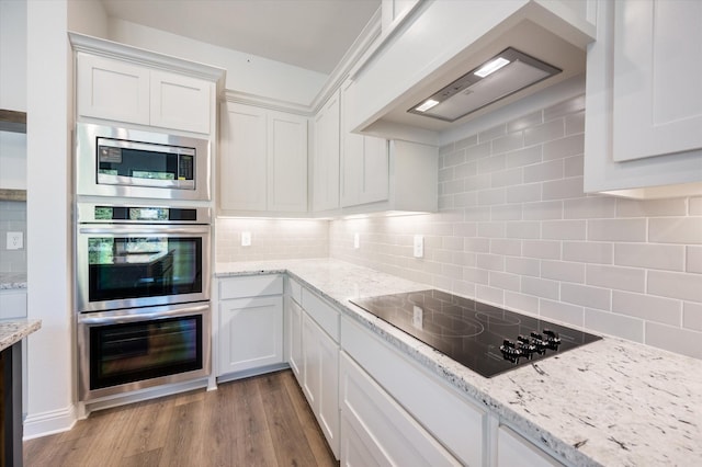 kitchen featuring light stone countertops, appliances with stainless steel finishes, white cabinets, custom range hood, and light wood-type flooring