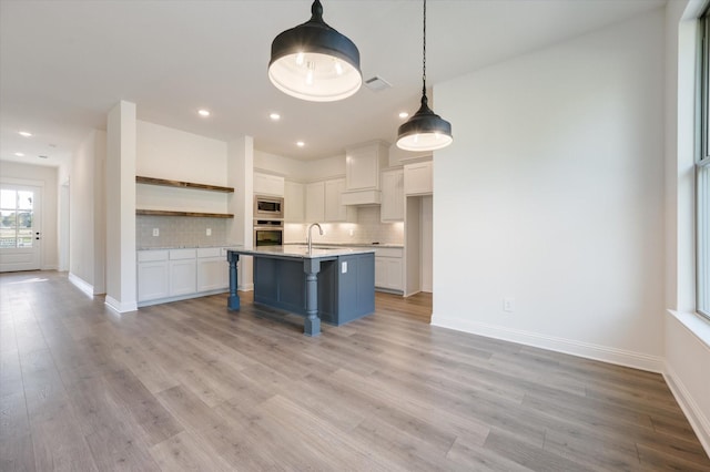 kitchen with appliances with stainless steel finishes, white cabinetry, backsplash, a kitchen breakfast bar, and a center island with sink