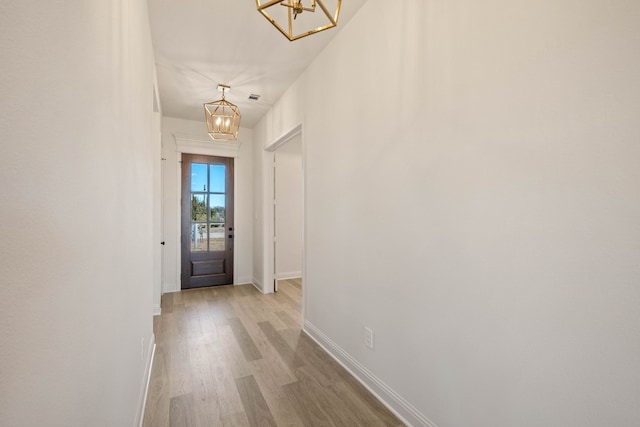 doorway featuring baseboards, light wood finished floors, and an inviting chandelier