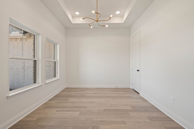 empty room with light wood-style floors, baseboards, a raised ceiling, and recessed lighting