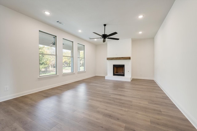 unfurnished living room with ceiling fan, a large fireplace, and light wood-type flooring