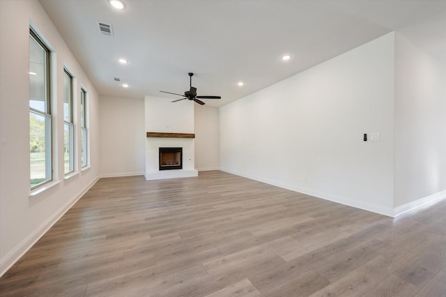 unfurnished living room featuring ceiling fan, a fireplace, and light wood-type flooring