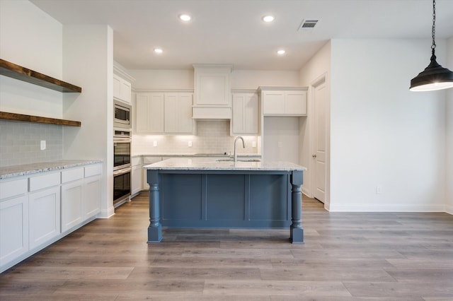 kitchen featuring decorative light fixtures, stainless steel microwave, white cabinetry, and light stone counters