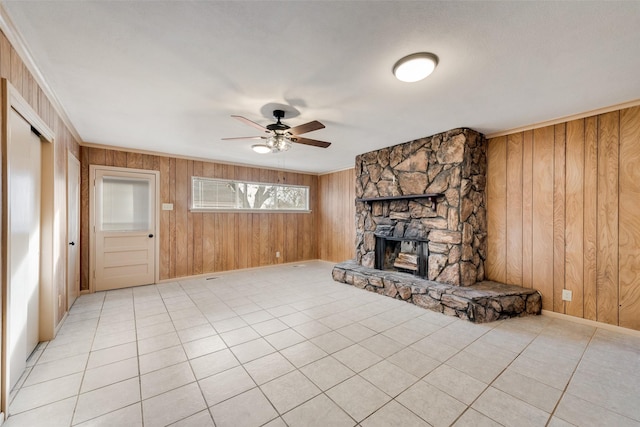 unfurnished living room featuring a stone fireplace, wooden walls, ceiling fan, and light tile patterned floors